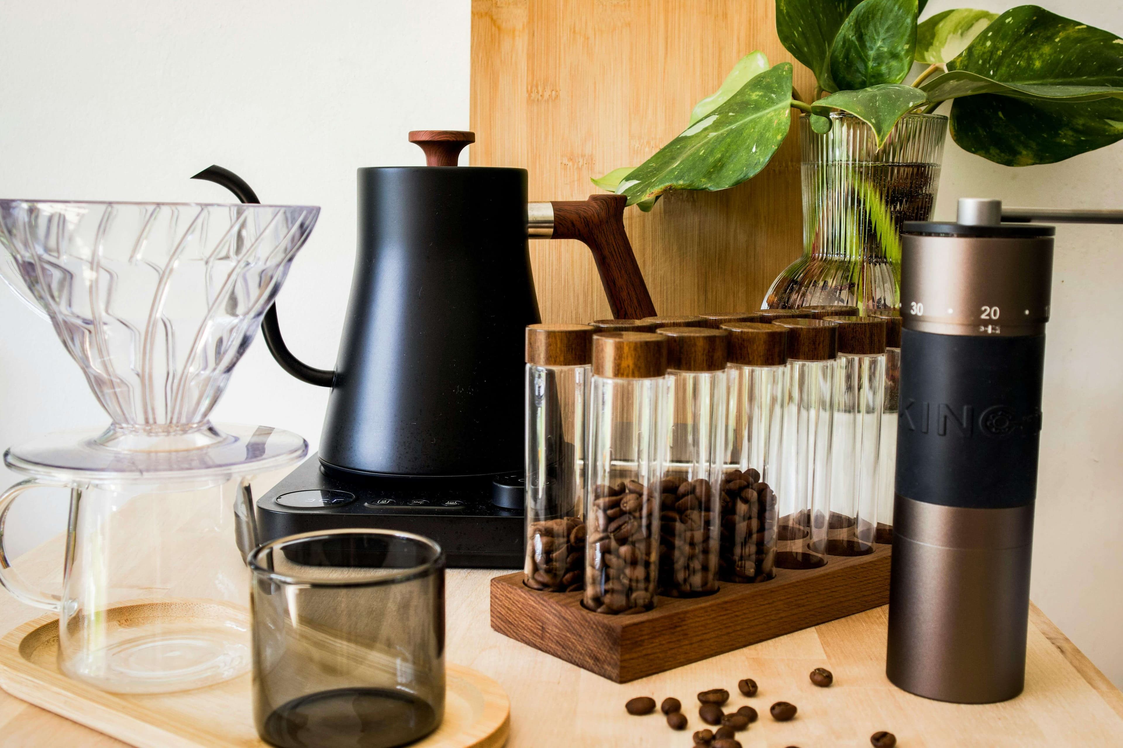 A home brewing setup on a wooden counter: pour-over dripper, gooseneck kettle, a single-dose bean cellar, and a hand grinder